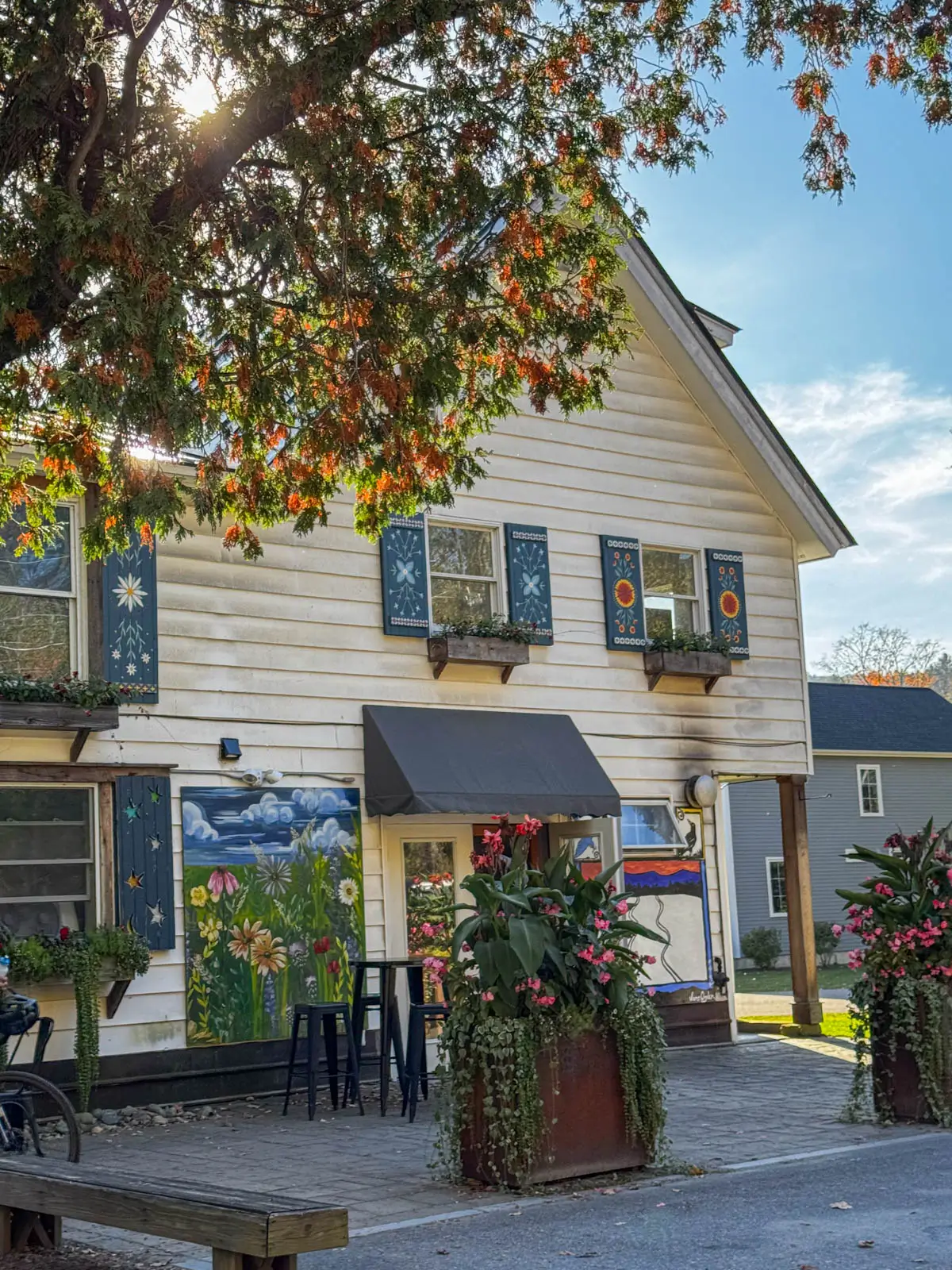 white colonial house part of edelweiss mountain deli in stowe vermont with orange leaf tree framing the house on the left.