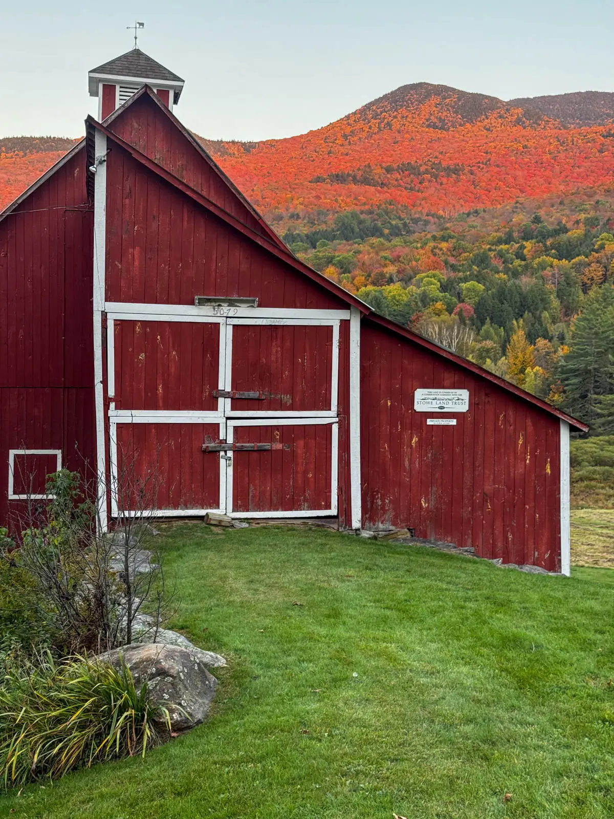 big red barn at sunset time in stowe vermont with orange colored mountain range behind it in fall.