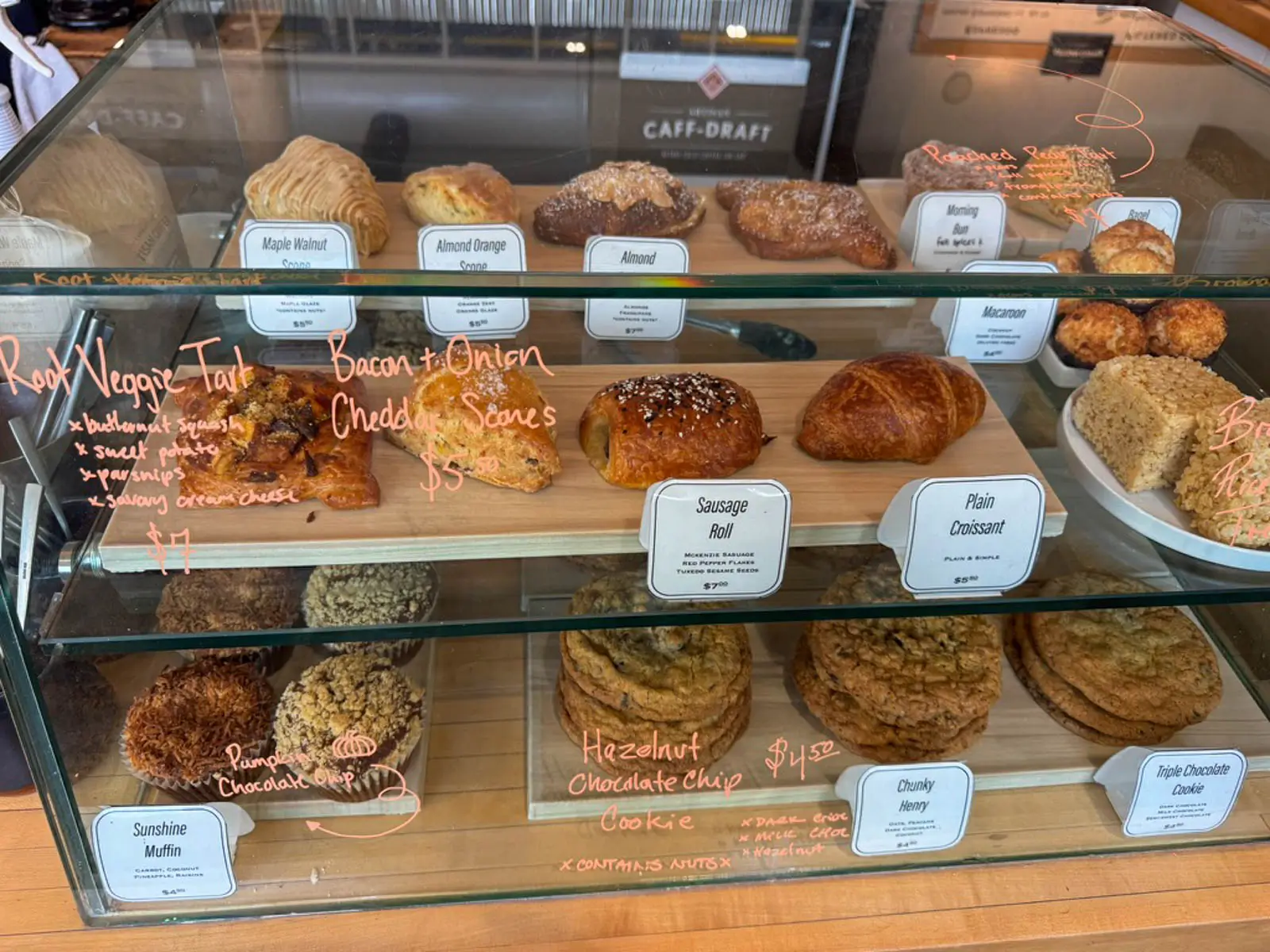 array of baked goods like croissants and cookies in a glass case on wooden shelves.