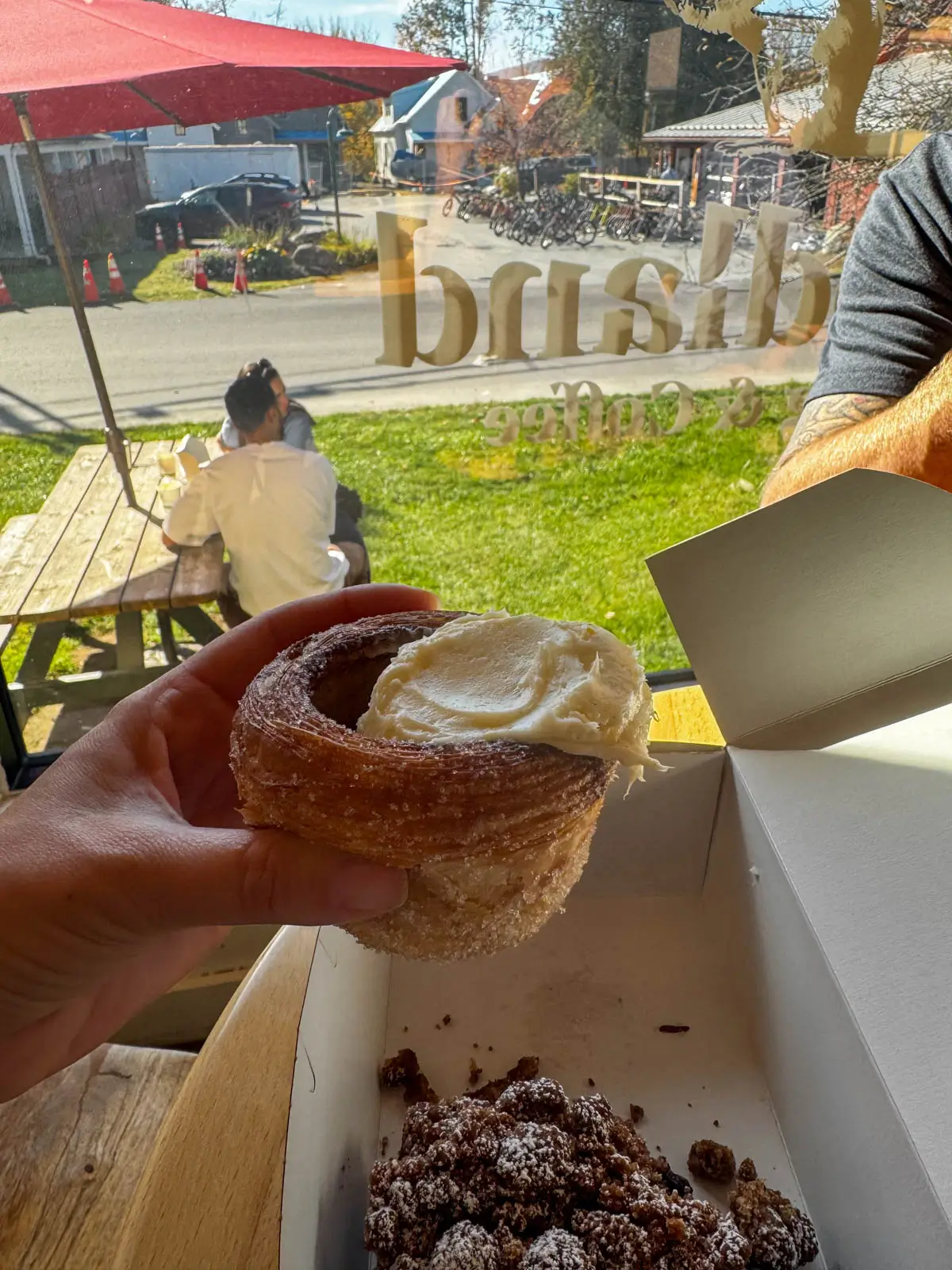 a white woman's hand holding a cinnamon roll with white frosting on top.