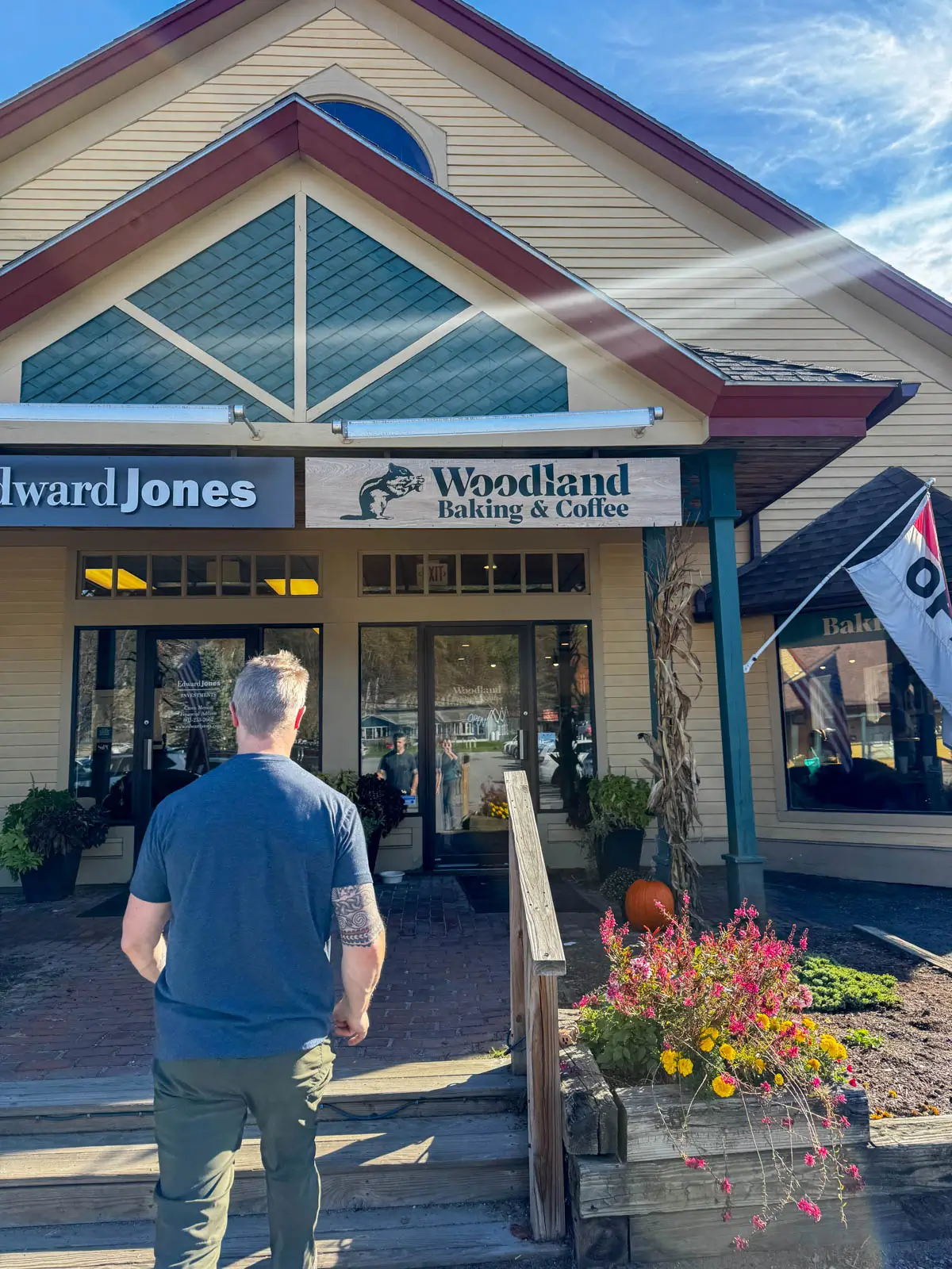 back of a man in gray t-shirt and green hiking pants walking into a building that says "woodland baking & co" on a sunny day with an "open" flag in the front.