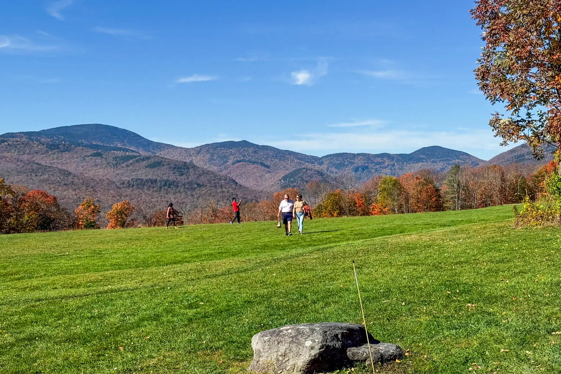 wide open green lawn in the fall with two people in white shirts walking in the distance with orange covered mountain range in distance in fall in stowe vermont.