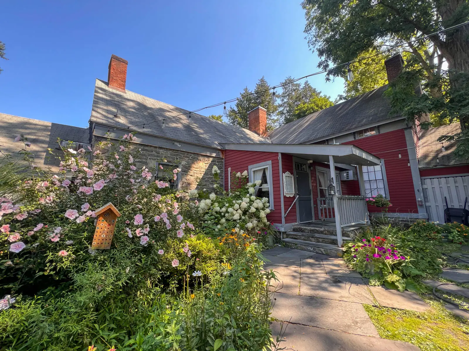 garvans gastropub restaurant wth charming red cape house and lots of plants, hydrangeas, and flowers outside in front with clear blue sky above.