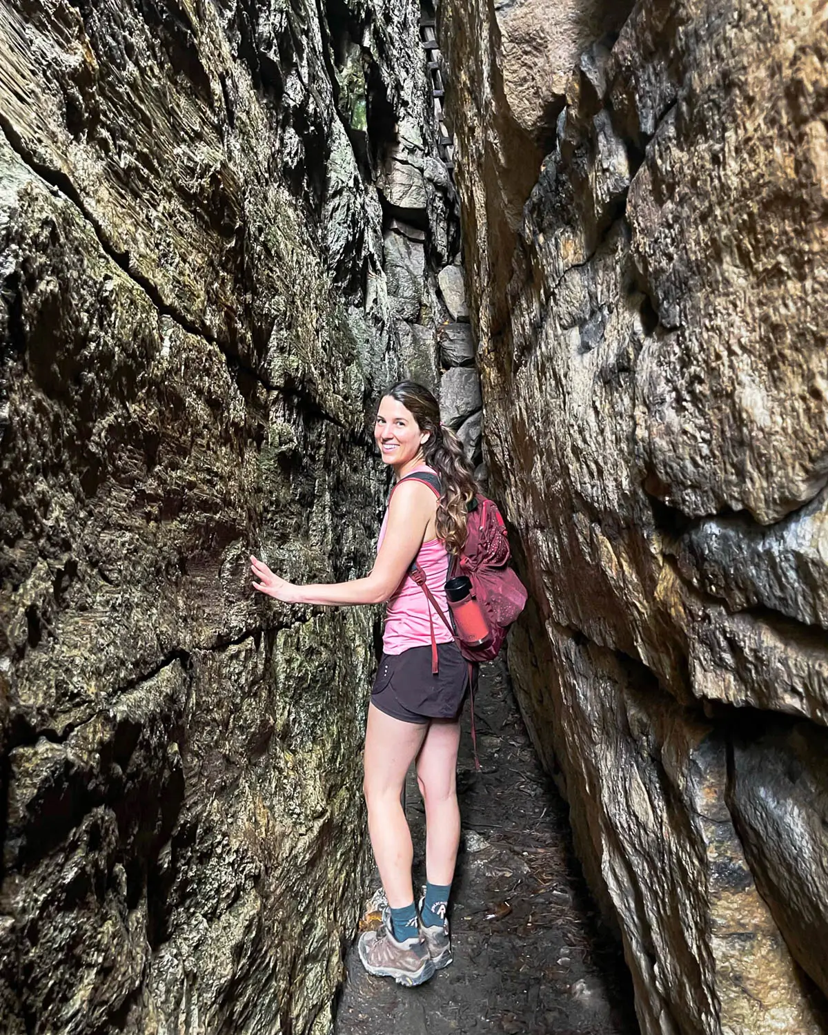woman in pink tank top and maroon shorts walking through slabs of rock on the lemon squeeze hike in new paltz.