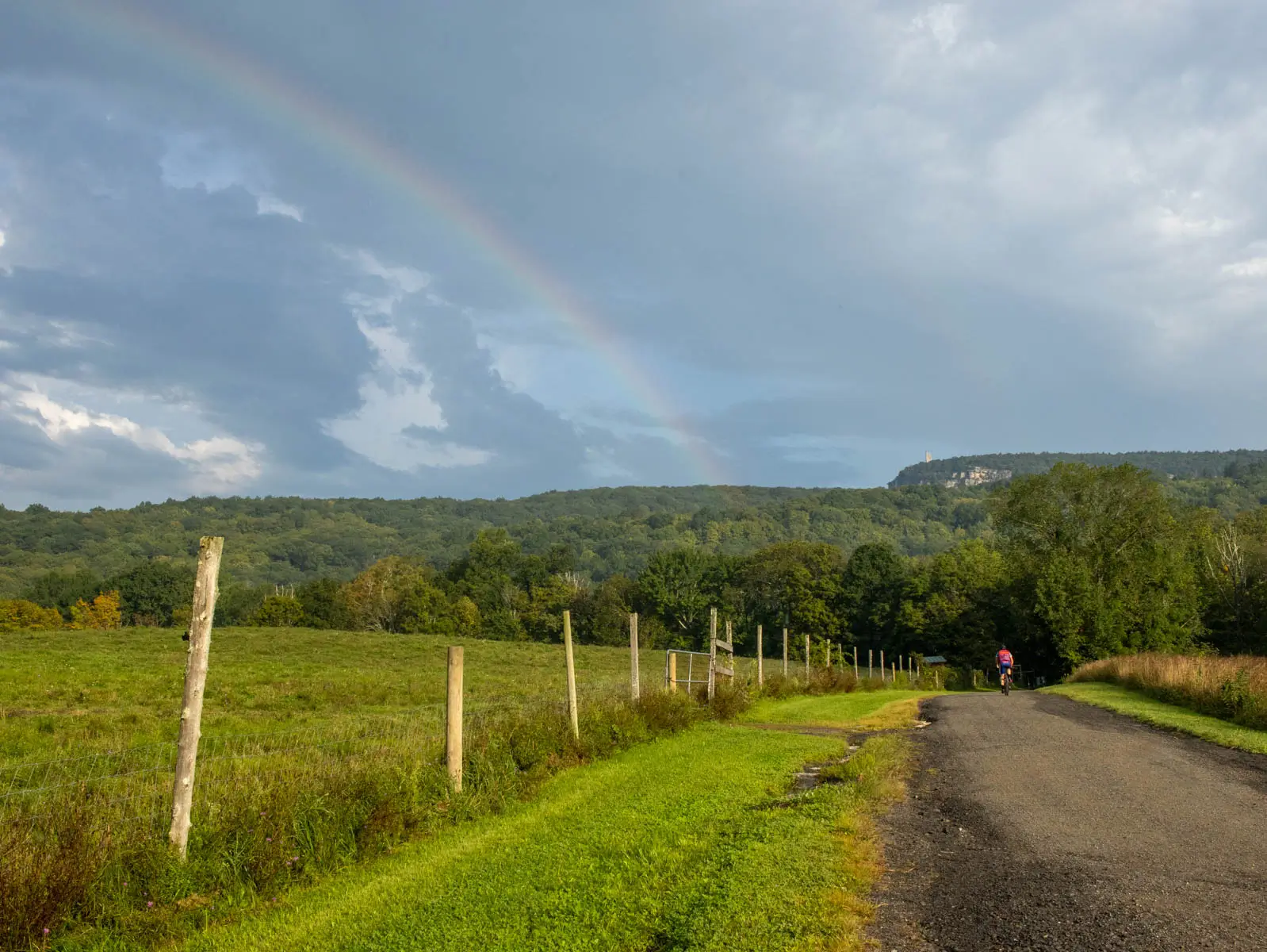 a rainbow over the shawangunk ridge in new paltz on a summer morning with rolling green mountain ridge in distance and gold grass and meadows in front.