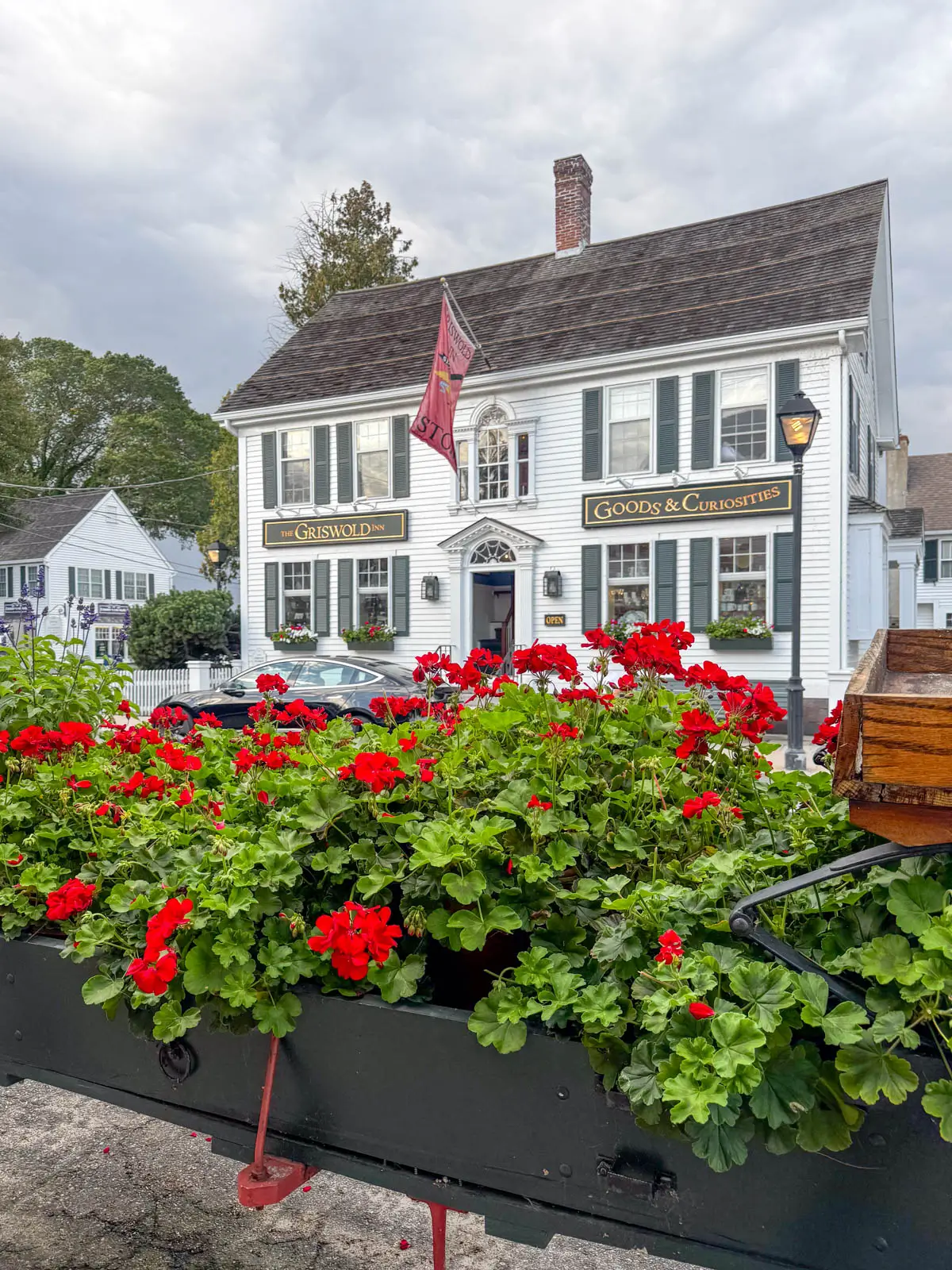 white colonial storefront with "griswold" with bunches of red flowers in front of it.
