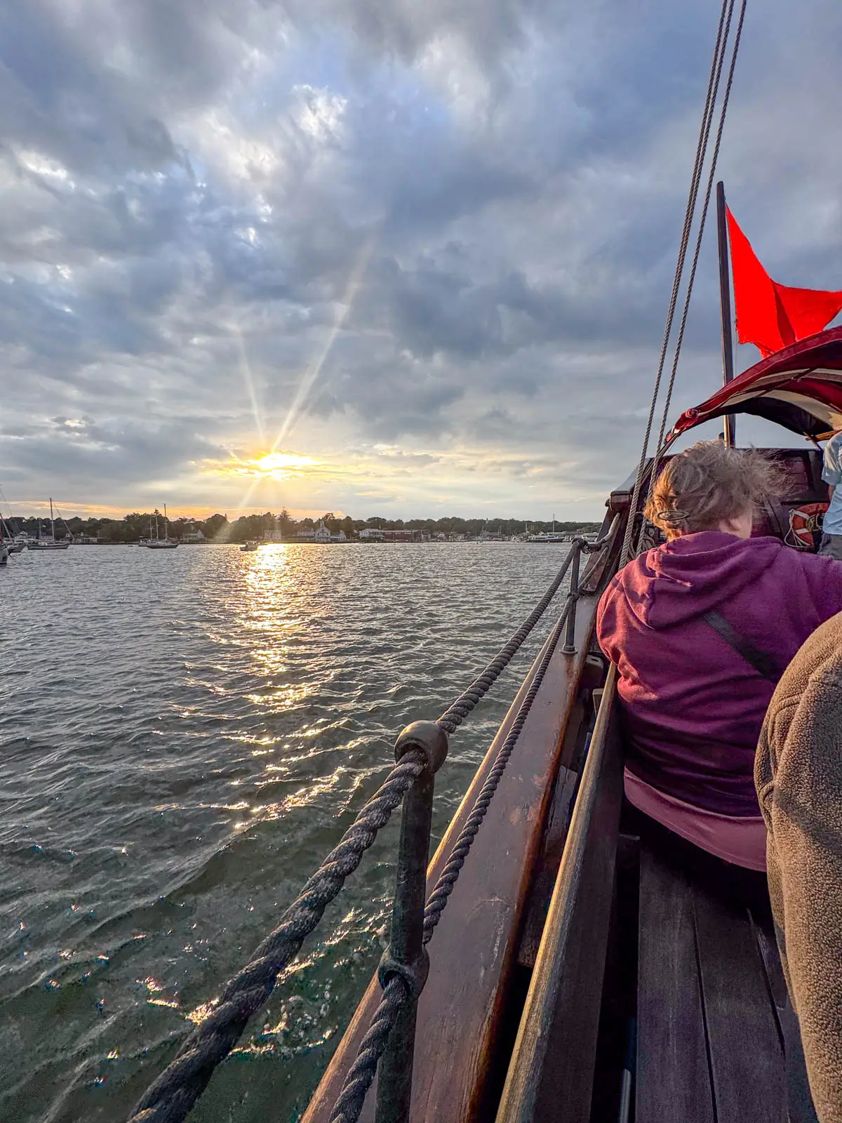 view from a boat at sunset time looking out at the water and a golden sun shining through the clouds in the distance.