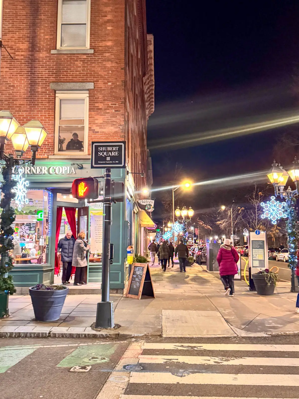 downtown New Haven at night in winter with people walking bundled in jackets and lampposts decorated with christmas lights and lit up snowflakes.