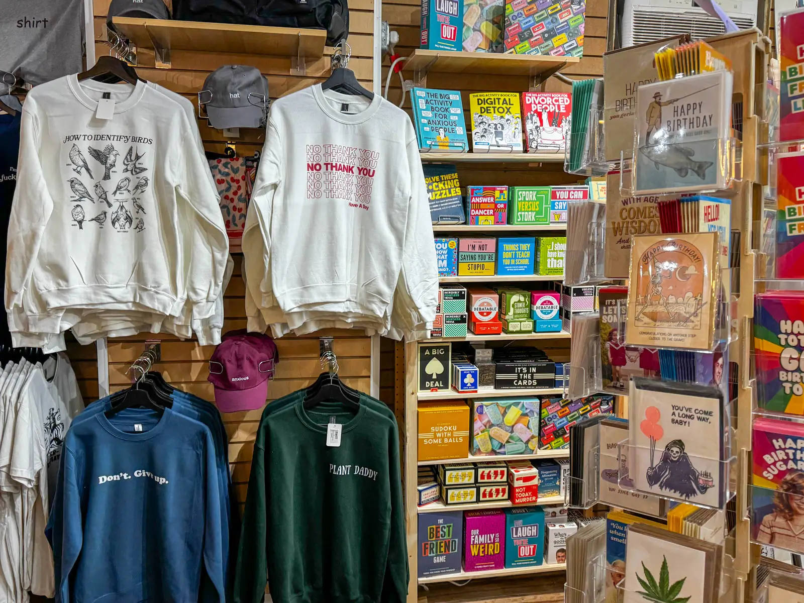 array of goods inside a store in Mystic Connecticut with sweatshirts lining the wooden wall and a shelf of cards and games to the right.